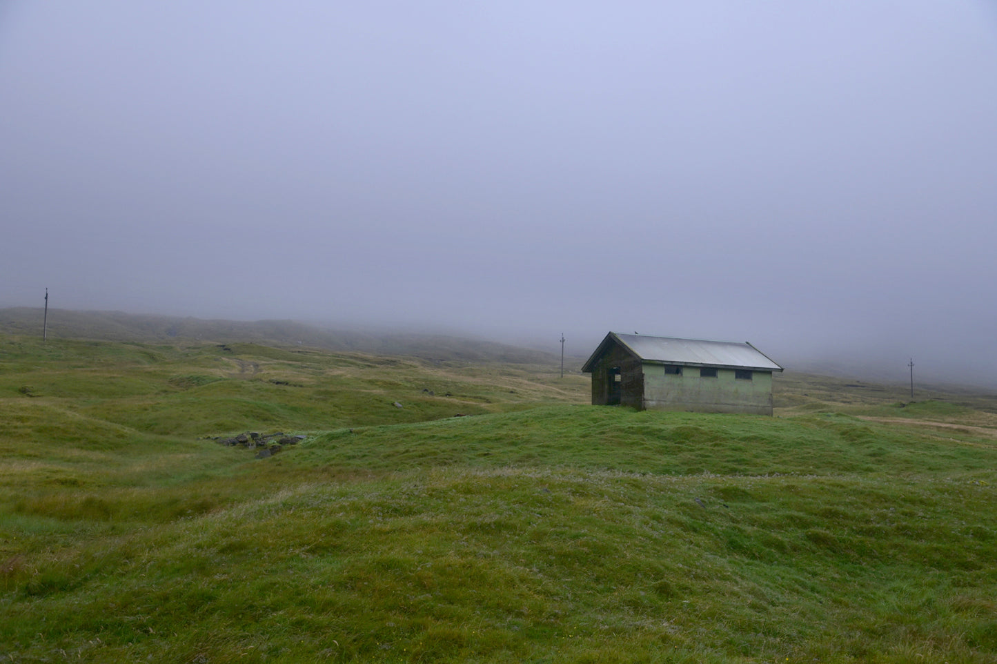 Beautiful, tiny green shed on the cliffs of the Faroe Islands, surrounded by fog. Fine art photography by Kristen Olivares.