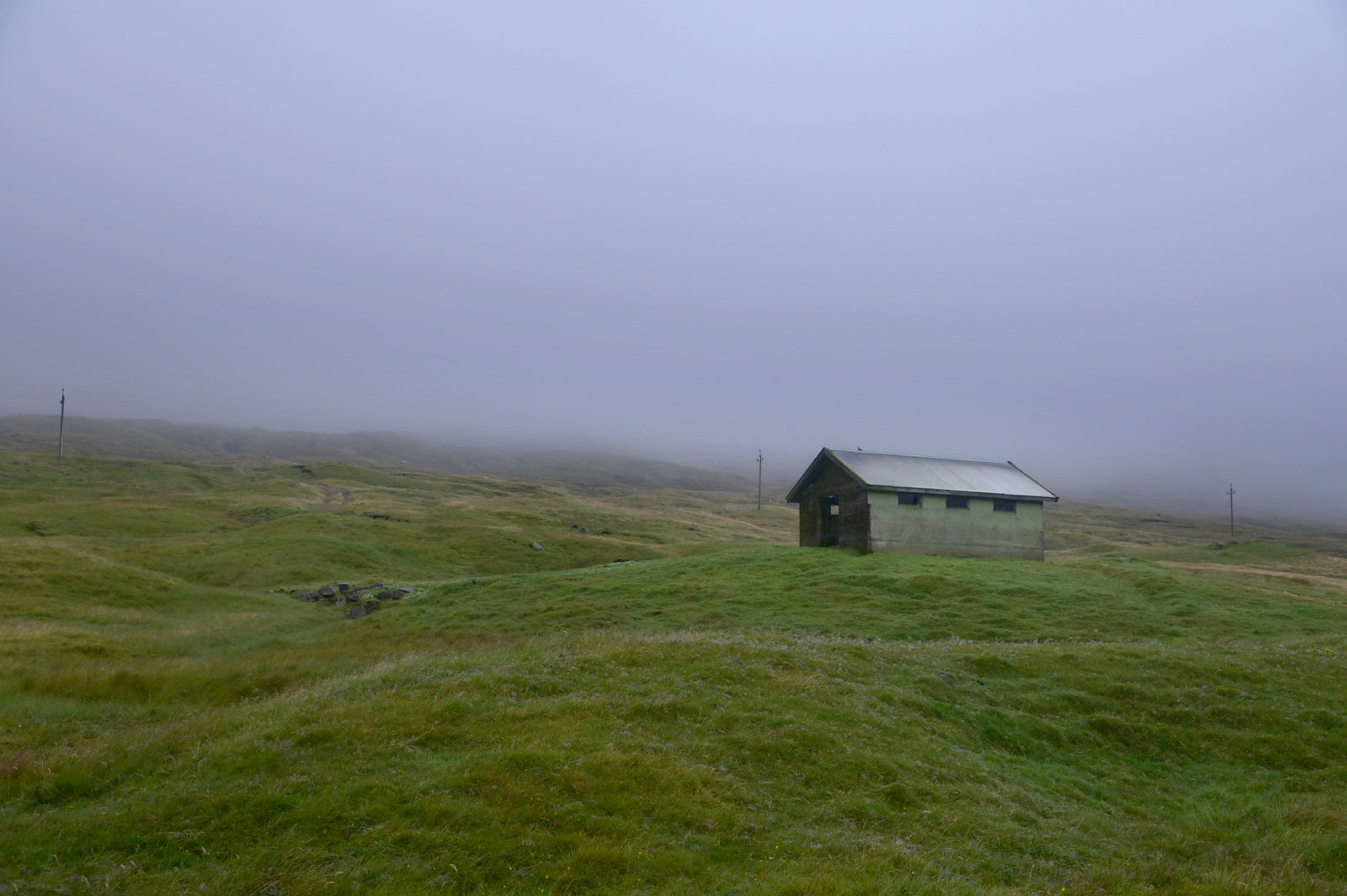 Beautiful, tiny green shed on the cliffs of the Faroe Islands, surrounded by fog. Fine art photography by Kristen Olivares.