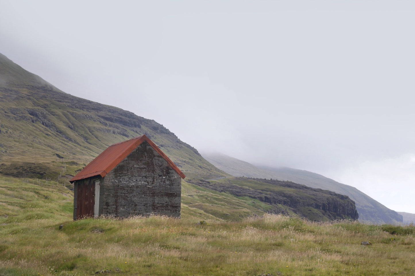 An old stone shack with a rusty colored roof set in the desolate foggy land of the Faroe Islands. Framed fine art photography by Kristen Olivares.